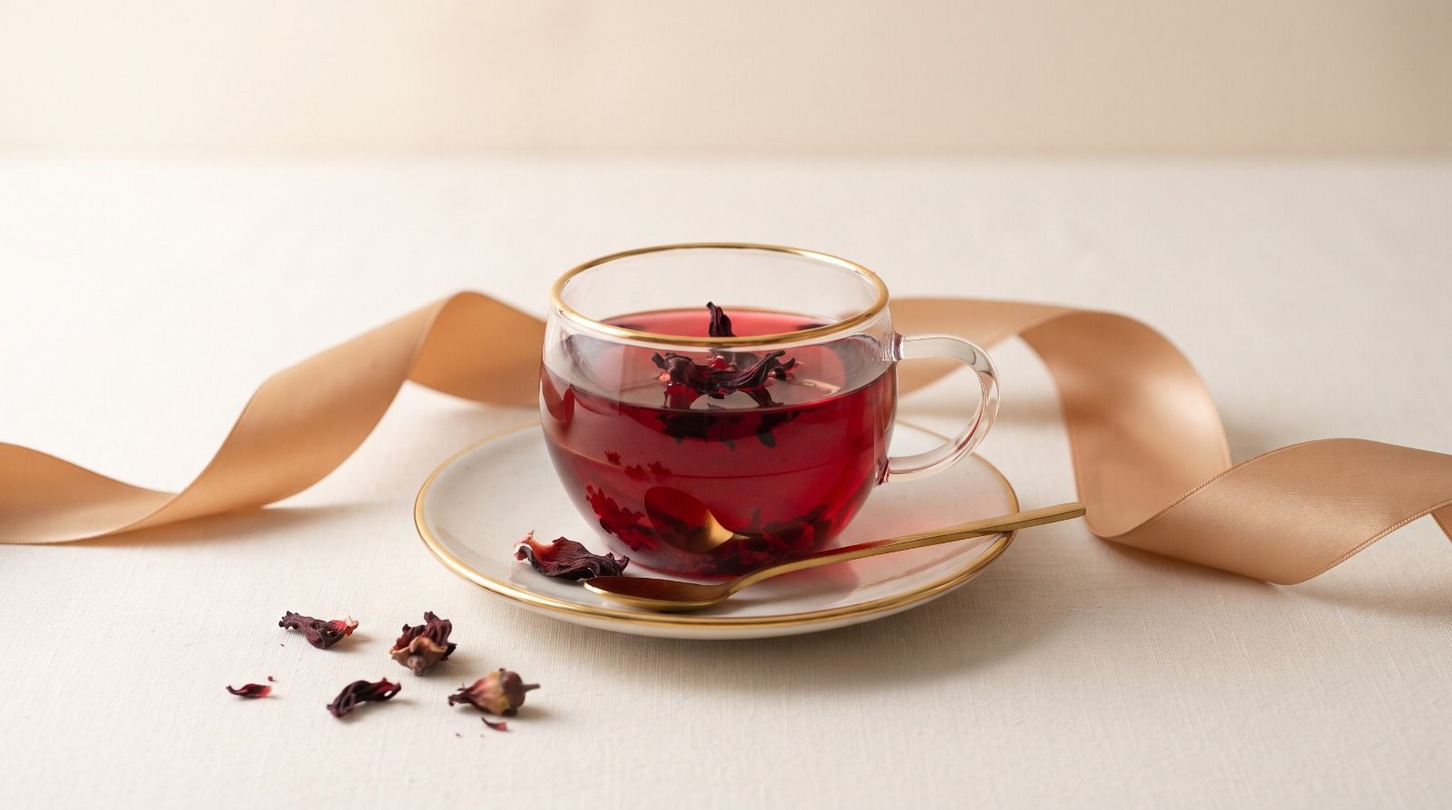 A glass cup of deep ruby hibiscus tea with dried hibiscus flowers on the saucer